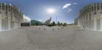 some birds and a person in a large circle on the sidewalk near buildings with sun on sky