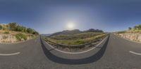 the view of a mountain pass from inside a 360 - eye lens camera screen shows a straight road with a curved bend and trees on either side