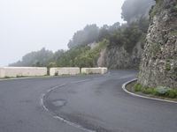 two winding roads with trees and fog on the cliff side next to the road, in the mountains