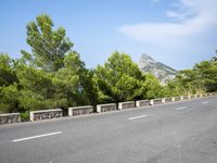 an empty road between two wooded hills and bushes on either side of the road is a steep hill with a steeped top