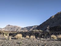 the man rides his skate board on the rocks near a mountain valley and dry grass