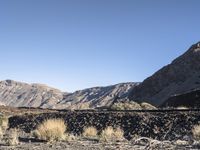 the man rides his skate board on the rocks near a mountain valley and dry grass