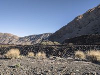 the man rides his skate board on the rocks near a mountain valley and dry grass