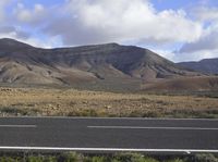 a view from the side of a road looking at a mountains range with sheep grazing on the side