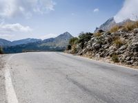 a long paved road leading into a mountain range in italy in the day time as the wind picks its ground