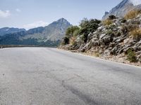 a long paved road leading into a mountain range in italy in the day time as the wind picks its ground