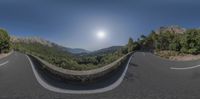 a curved road and a stone wall overlooking a mountain range on a sunny day, with the sun rising