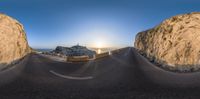 a long curved road through a mountain under a blue sky with sun setting in the distance