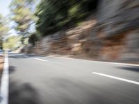 a blurred photo of a motorcycle and car going down a mountain side road towards trees