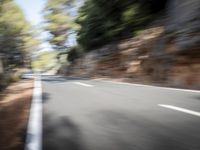 a blurred photo of a motorcycle and car going down a mountain side road towards trees