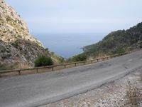 an open road next to a mountain area with trees and the ocean in the background