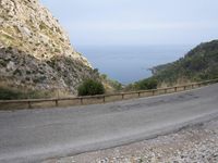 an open road next to a mountain area with trees and the ocean in the background