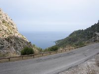an open road next to a mountain area with trees and the ocean in the background