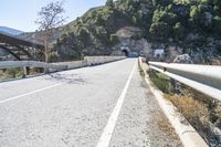 an empty road next to some hills under a bridge with a tunnel on the side