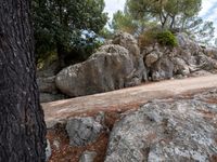 a mountain side with rock outcropping and pine trees in the distance near large boulders