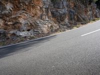 a lone motorcycle is parked at the side of a mountainous highway near a rock wall