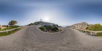 fisheye view of a winding road leading to a lighthouse with mountains in the background