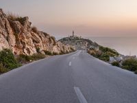 this is a scenic view of a road with a light house in the distance on a cliff