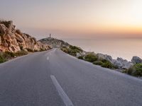 this is a scenic view of a road with a light house in the distance on a cliff