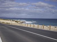 a wide road is shown with ocean and sky in the background while driving away from it