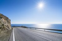 a long empty road with a sun on the side of it and an ocean in the background