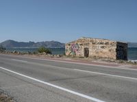 a graffiti covered building is by the edge of a beach road by the ocean in a coastal area