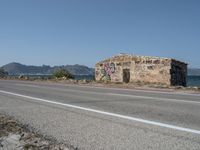 a graffiti covered building is by the edge of a beach road by the ocean in a coastal area