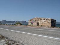 a graffiti covered building is by the edge of a beach road by the ocean in a coastal area