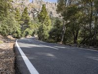 a motorcycle is stopped on a empty road in front of a rocky cliff and treeline