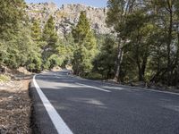 a motorcycle is stopped on a empty road in front of a rocky cliff and treeline