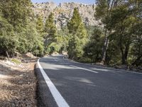 a motorcycle is stopped on a empty road in front of a rocky cliff and treeline