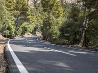 a motorcycle is stopped on a empty road in front of a rocky cliff and treeline