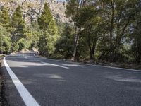 a motorcycle is stopped on a empty road in front of a rocky cliff and treeline