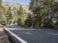 a motorcycle is stopped on a empty road in front of a rocky cliff and treeline