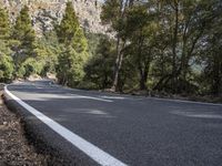 a motorcycle is stopped on a empty road in front of a rocky cliff and treeline