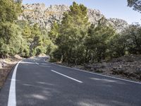 a motorcycle is stopped on a empty road in front of a rocky cliff and treeline