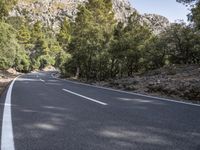 a motorcycle is stopped on a empty road in front of a rocky cliff and treeline