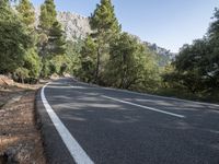 a motorcycle is stopped on a empty road in front of a rocky cliff and treeline