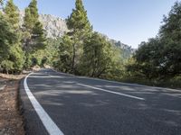 a motorcycle is stopped on a empty road in front of a rocky cliff and treeline