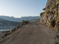 a person on their bike riding down a long cliff side road next to a body of water