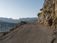 a person on their bike riding down a long cliff side road next to a body of water