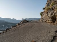 a person on their bike riding down a long cliff side road next to a body of water