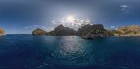 a boat sails in blue water by some rocky islands with sun shining through the clouds