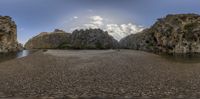 the view of an old river from a fish - eye perspective at a wide angle with rocks, gravel and trees