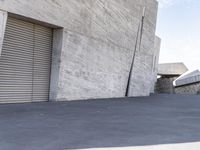 a skateboarder is going down the street in front of an industrial building with shutters