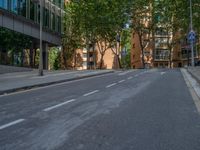 a paved road surrounded by trees in the city street, with people on bicycles on one side, and tall buildings on another side