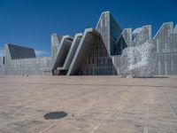 a white building with several steps and large glass panels in the facade is a mosaic that depicts a man