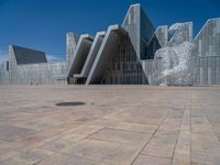 a white building with several steps and large glass panels in the facade is a mosaic that depicts a man