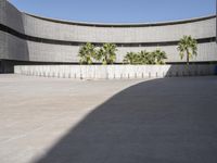 an empty courtyard with cement walls and palm trees in the foregrounds and blue sky