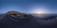 a large long winding road near the ocean at sunset and the sun setting over the horizon